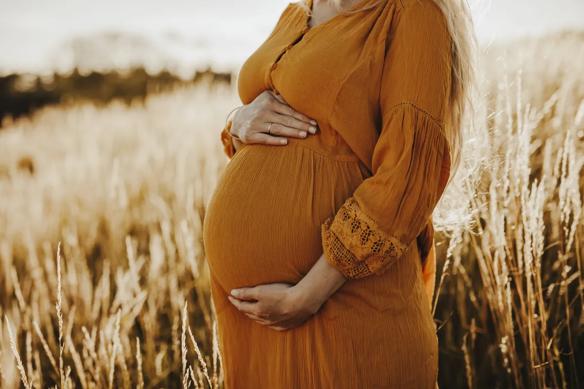Nærbilde av hender som holder rundt en gravid mage i oransje kjole