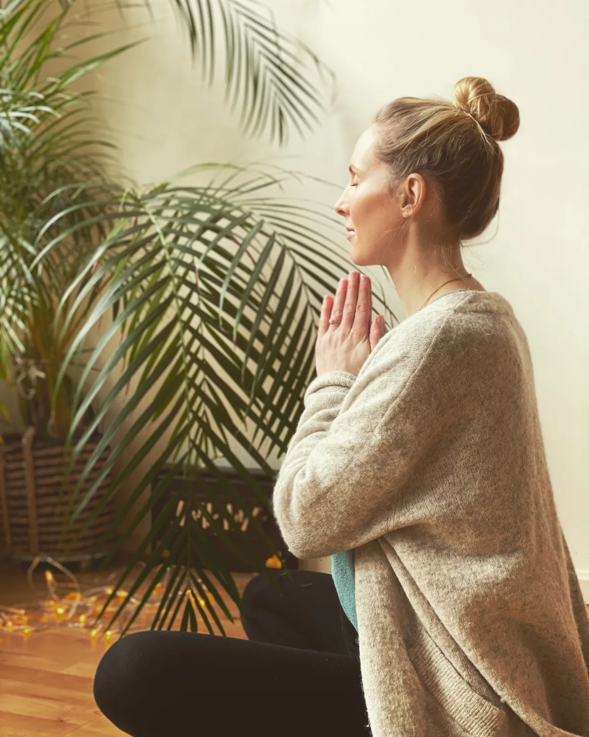 Mia sitter med hendene samlet foran brystet ved en stor palme i yogastudioet