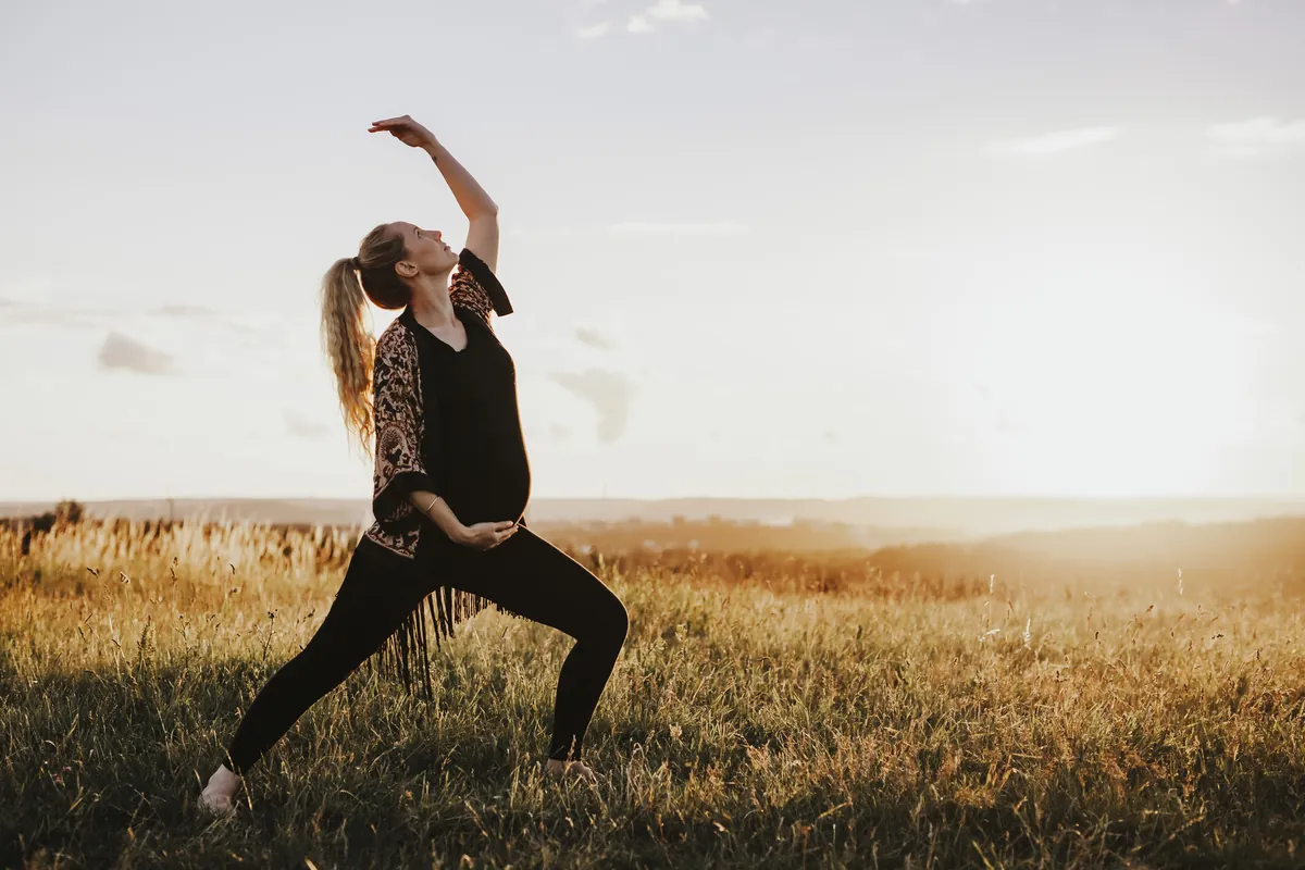 Gravide Mia i en flytende yogastilling med den ene armen over hodet